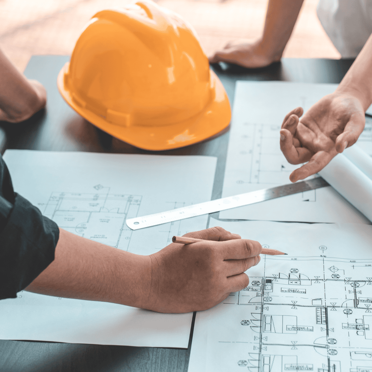 Two people reviewing architectural drawings at a table with a yellow hard hat.