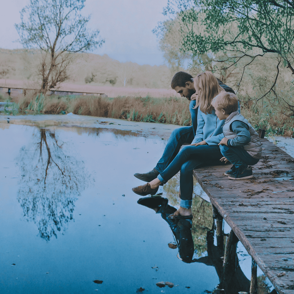 A family of three sitting on the edge of a wooden jetty by a calm lake. A family of three sitting on the edge of a wooden jetty by a calm lake.
